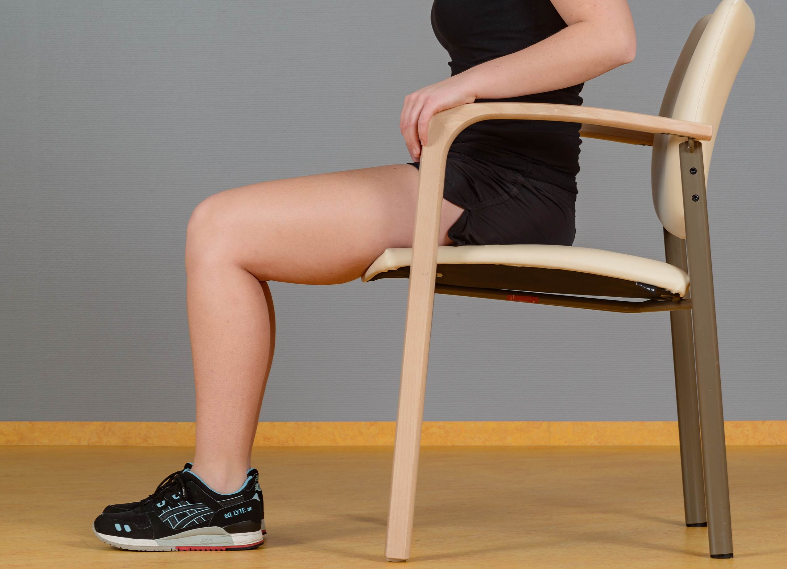 Oefening fysiotherapie zitten op stoel benen gebogen voeten op grond
