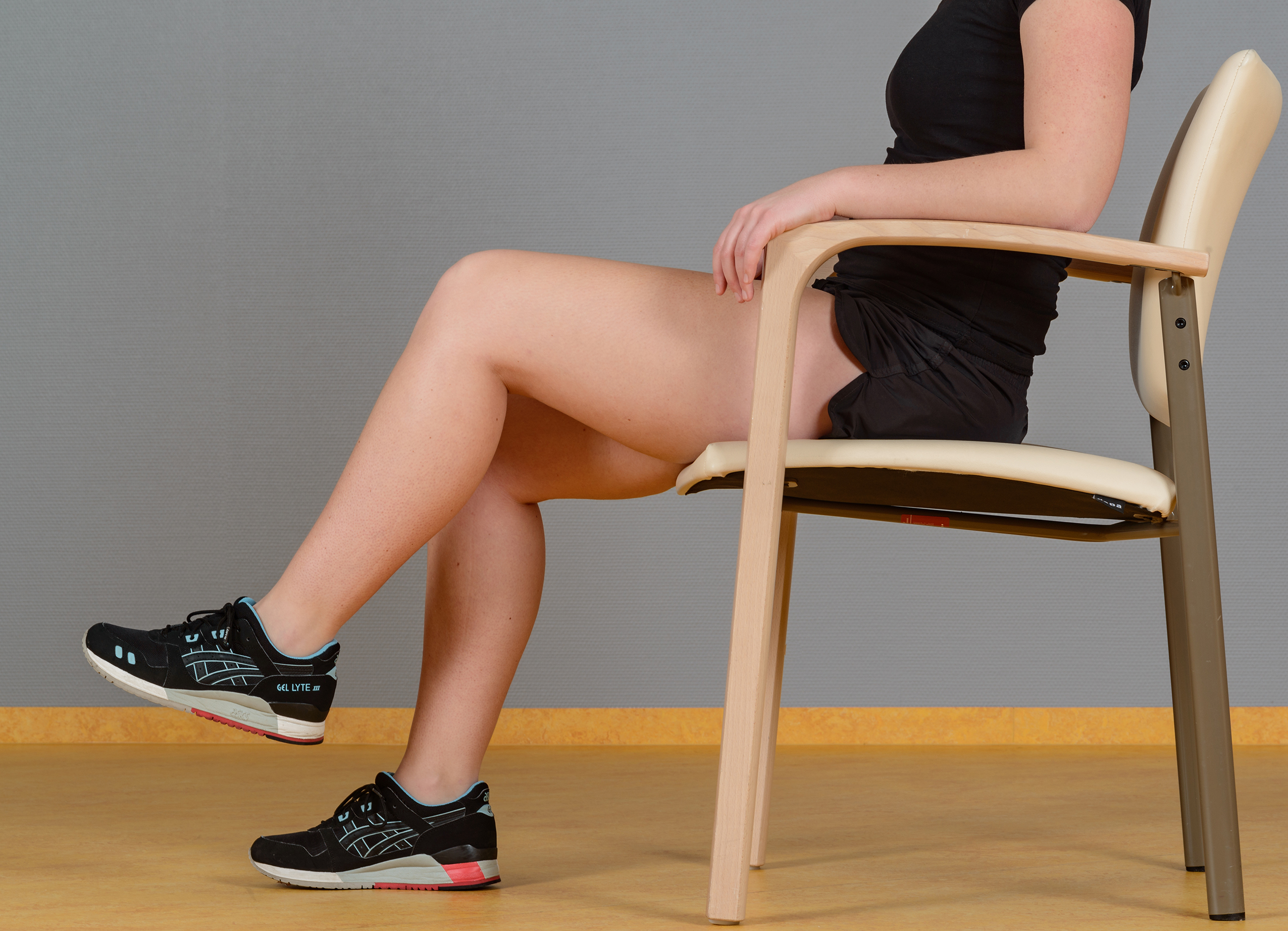 Oefening fysiotherapie op stoel knie optrekken