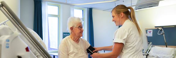 Verpleegkundige helpt patiënt aan bed